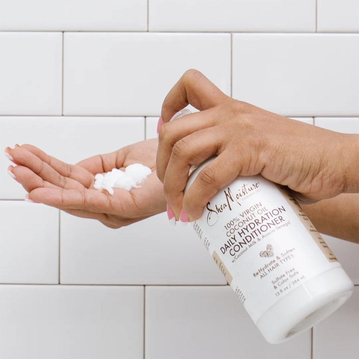 One hand holds a portion of Shea Moisture 100% Virgin Coconut Oil Daily Hydration Conditioner, 384ml. The balm is white and creamy.