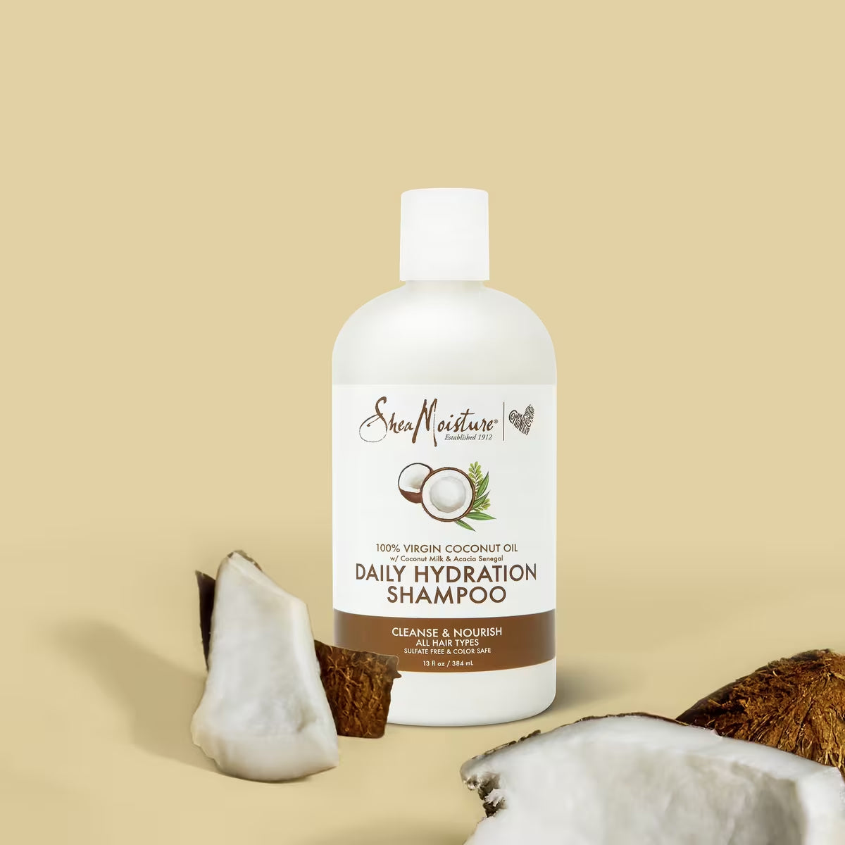 The product is Shea Moisture 100% Virgin Coconut Oil Daily Hydration Shampoo, 384ml. The shampoo is sulphate-free and colour-protecting, and it is suitable for all hair types. The bottle stands in front of a beige background with coconuts.