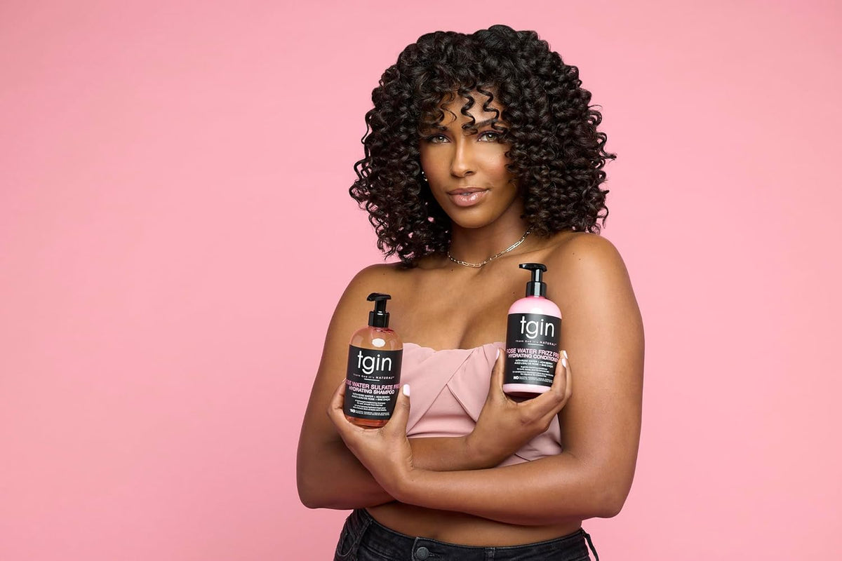 Woman with curly hair holding TGIN Rose Water Shampoo 384ml and conditioner in front of pink background.