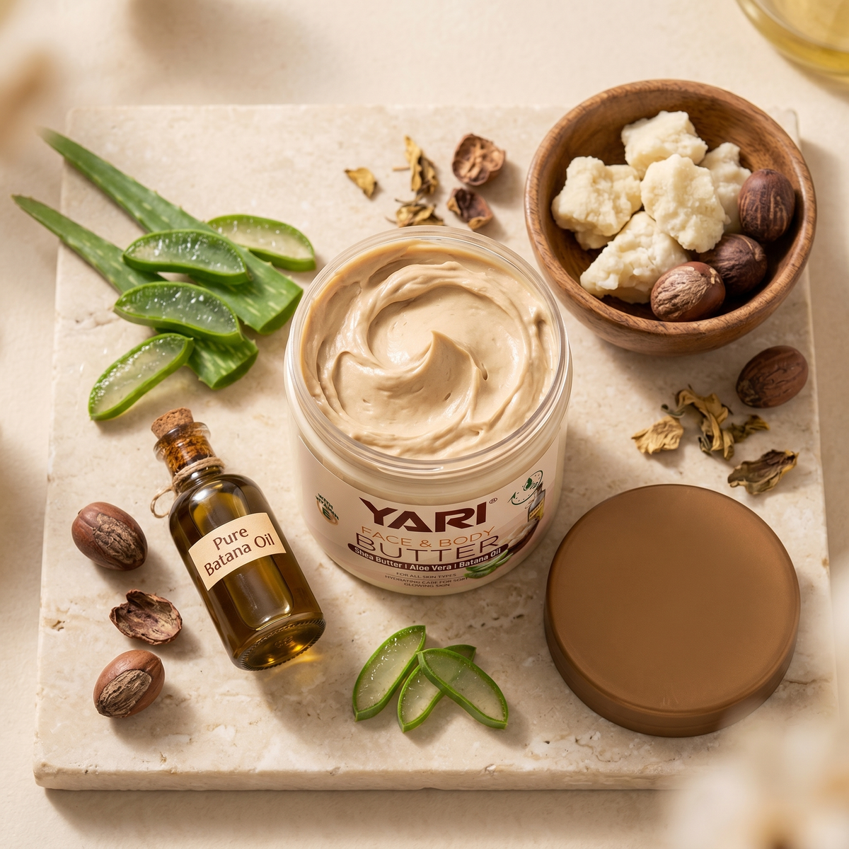 Yari Face & Body Butter with shea butter, aloe vera and batana oil surrounded by natural ingredients on a stone slab.